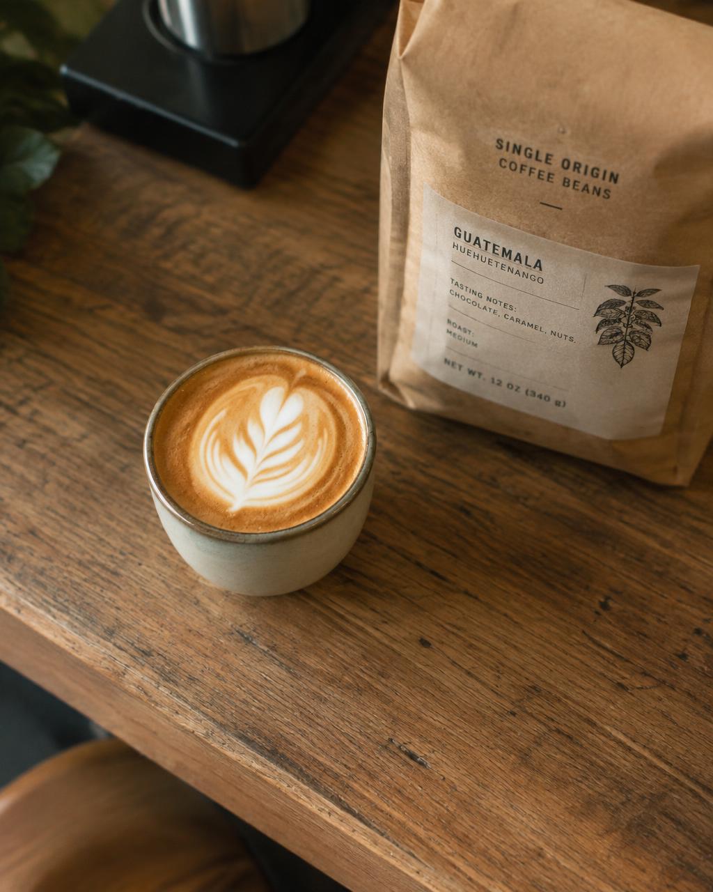 Cortado beside a bag of single-origin beans on an oak counter